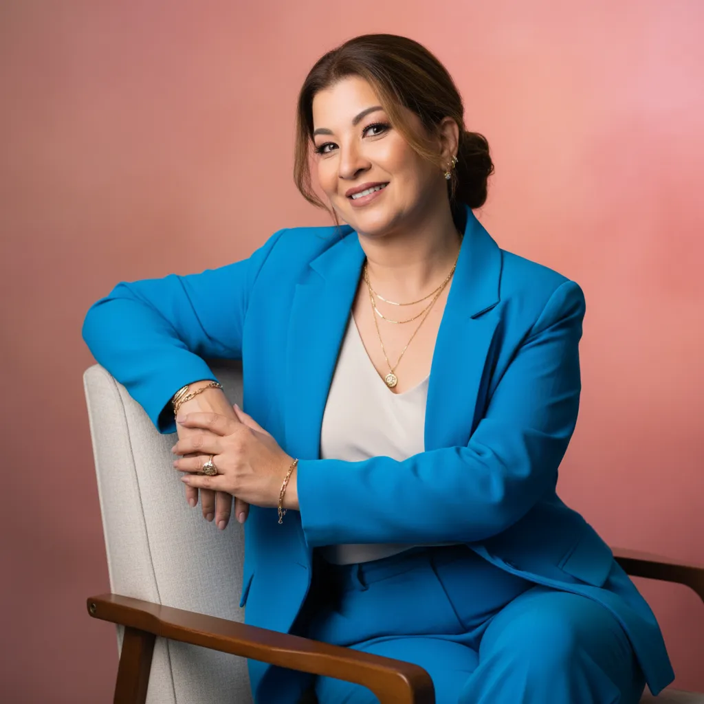 Anna Murakami sorrindo, de blazer azul, sentada em uma poltrona